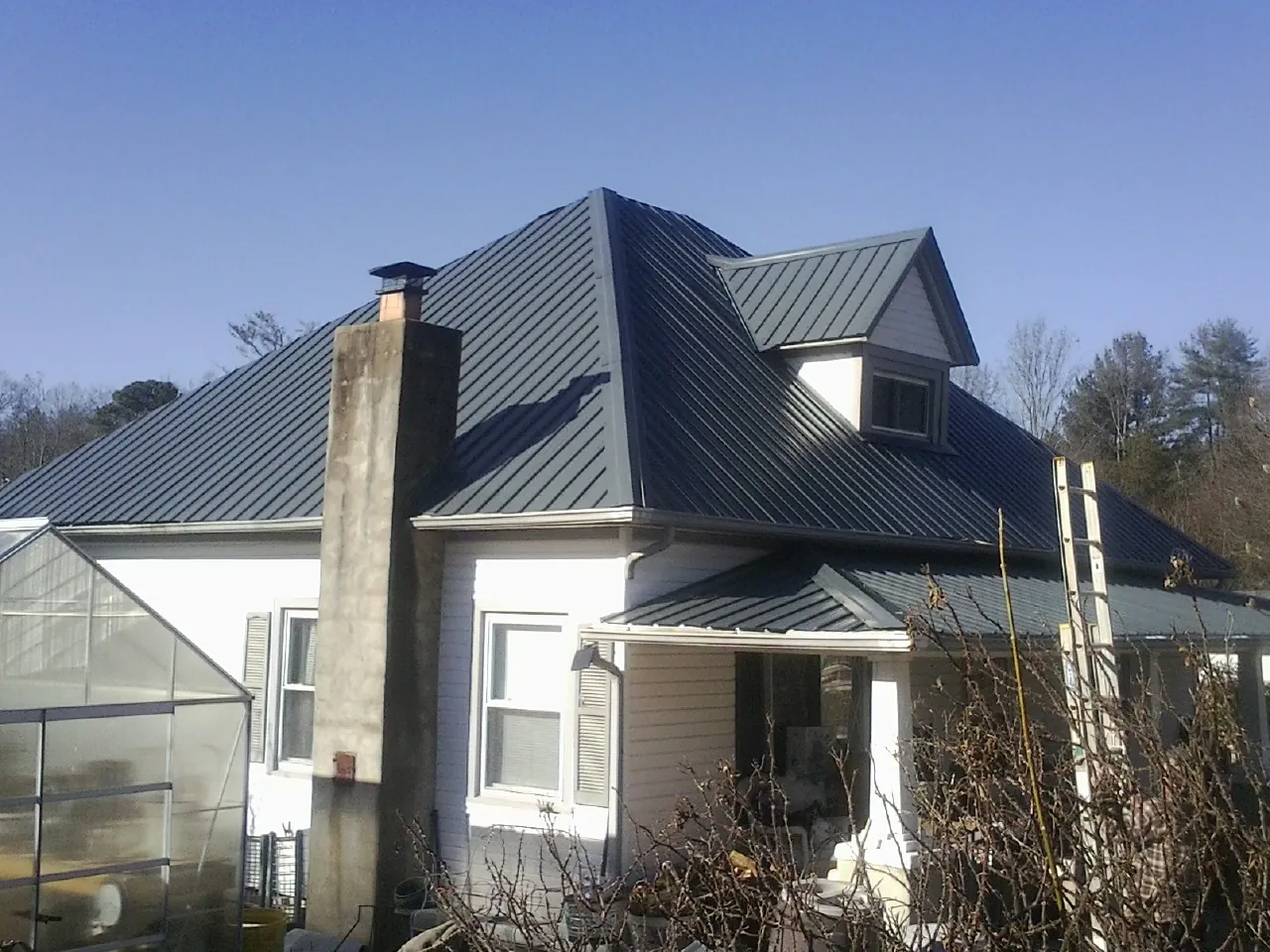 Dark blue standing seam metal roof on a white farmhouse with dormer — Slate & Tile Roof Repair by Roofing Brothers in Flint