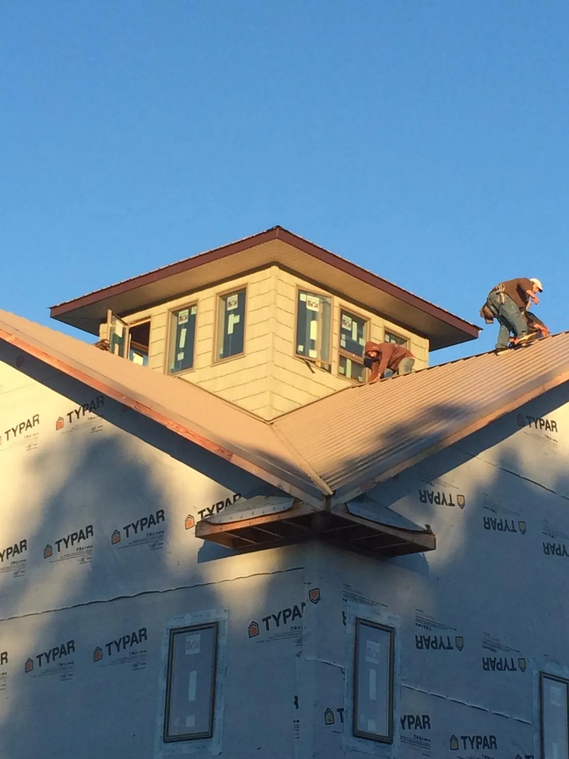 Roofers working around a rooftop cupola on a new metal roof at sunset — Roof Waterproofing in Flint by Roofing Brothers